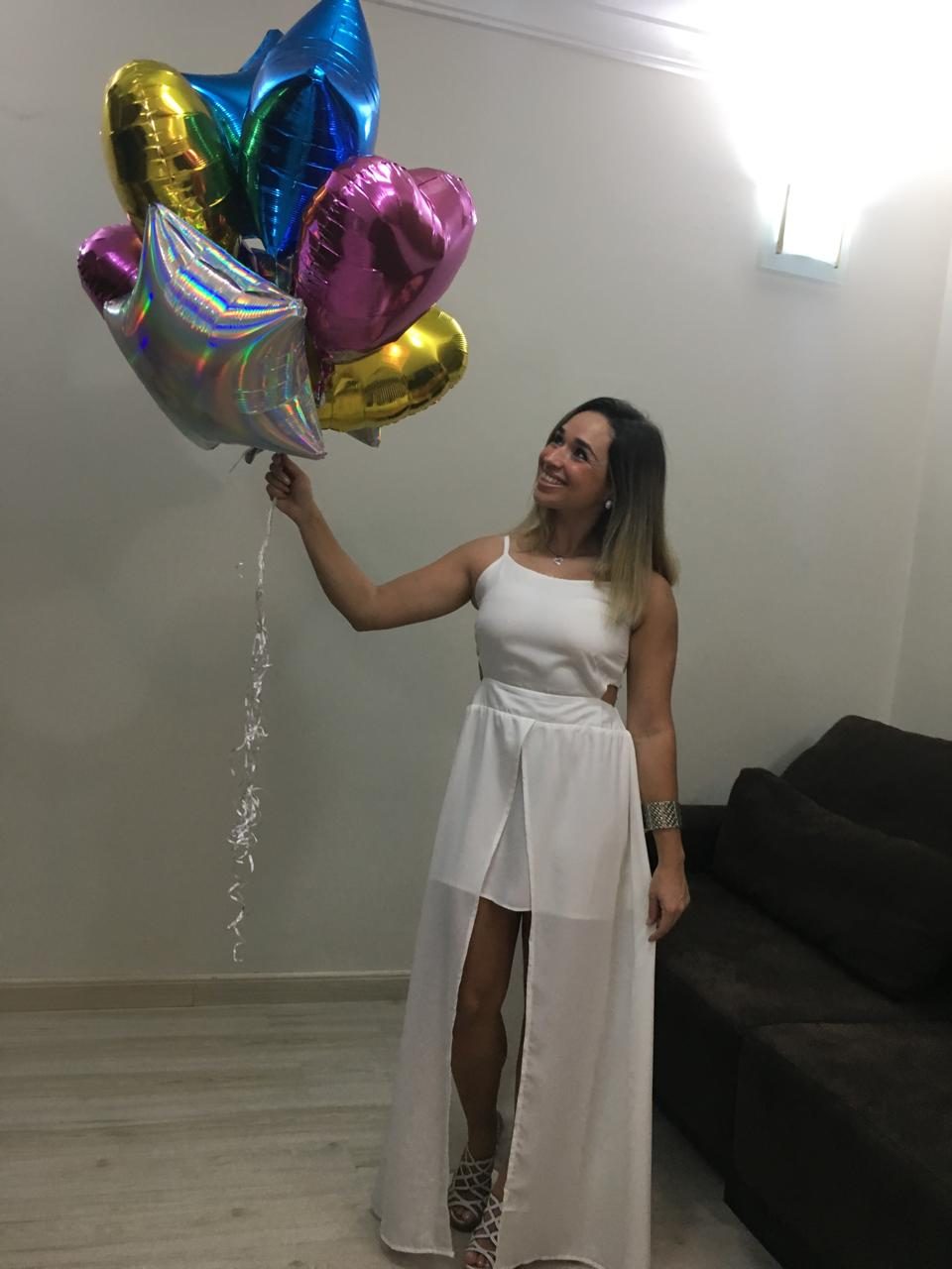 Luiza segurando um buquê de balões coloridos e olhando para cima com encanto
